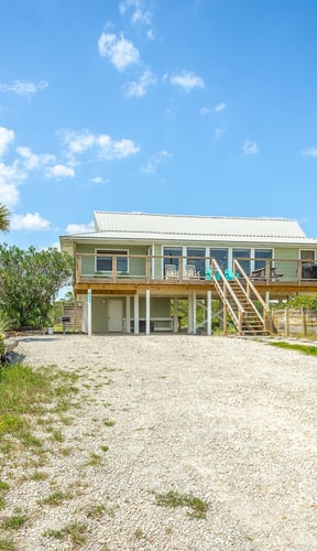 Beach house with elevated deck and palm trees on a sandy lot
