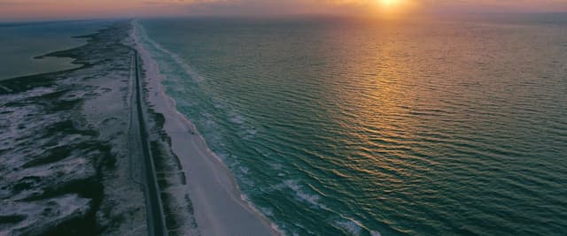 Aerial view of Florida panhandle barrier island at sunset, turquoise Gulf water and white sand stretching to the horizon